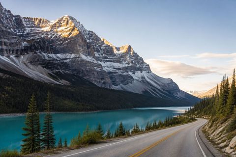 Mountain road beside a turquoise glacial lake and snow-capped peaks in the Canadian Rockies.