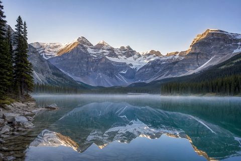 Turquoise glacial lake reflecting snow-capped Canadian Rocky Mountains in the early morning.